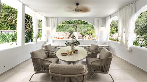 A sunlit room with a round table, four wicker chairs, a ceiling fan, and large windows with curtains. - Nama Summer Retreat Mikra Mantinia Beachfront Gem (Kalamata)