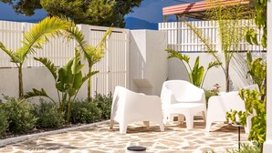 A patio with white chairs and tables, surrounded by greenery and a stone floor. - Nama Summer Retreat Mikra Mantinia Beachfront Gem (Kalamata)