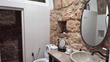 A bathroom with a stone wall, a white toilet, a sink with a marble basin, and a large mirror.
