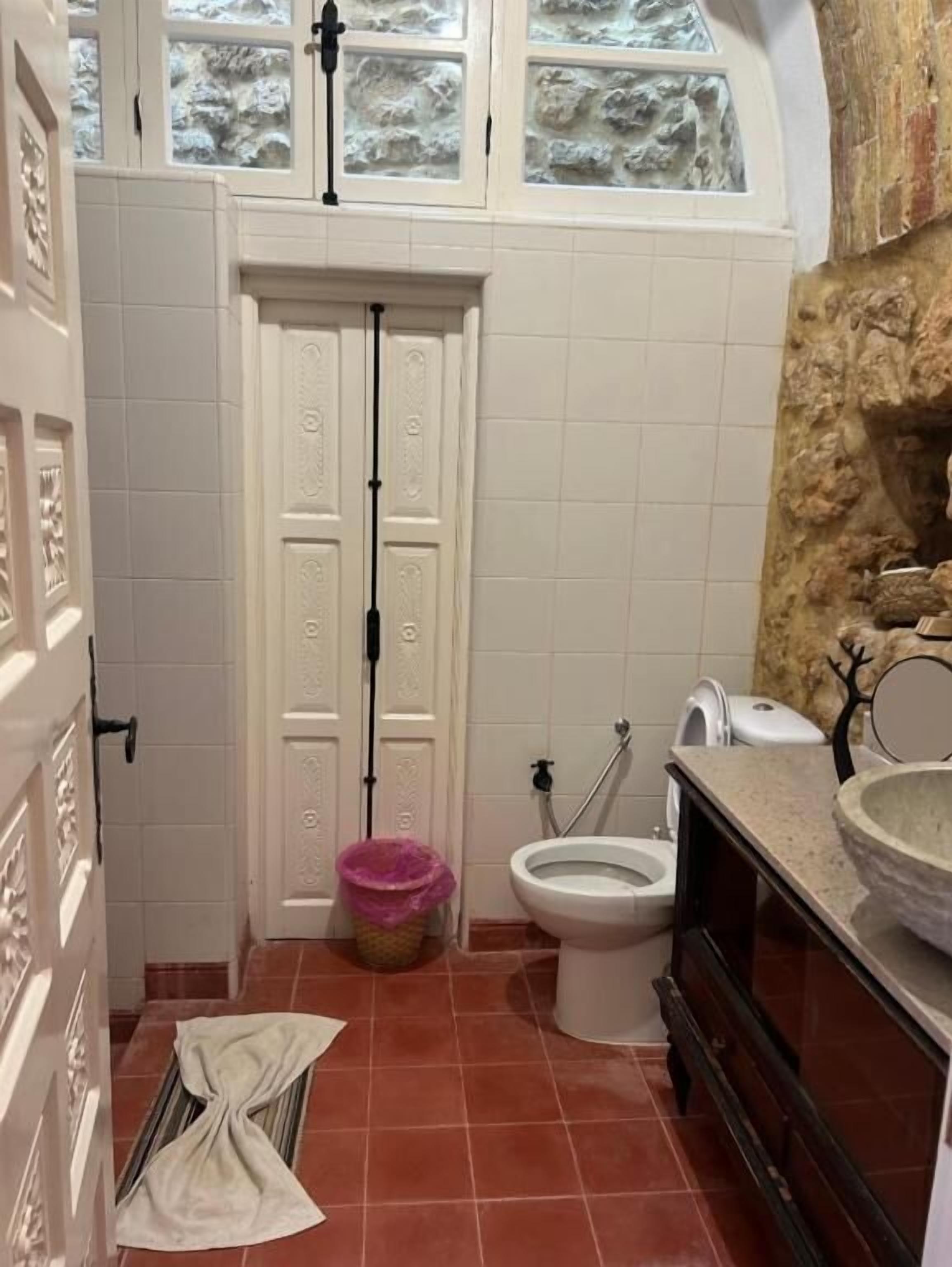 A bathroom with a white door, a toilet, a sink, and a window above the door.