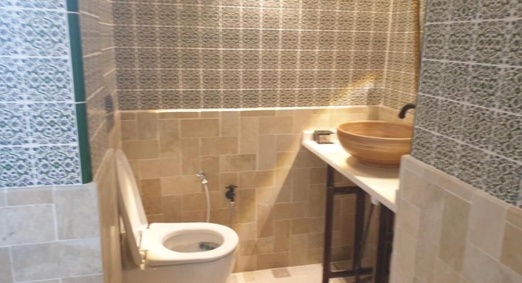 A small bathroom with a toilet, a sink with a bowl, and tiled walls.