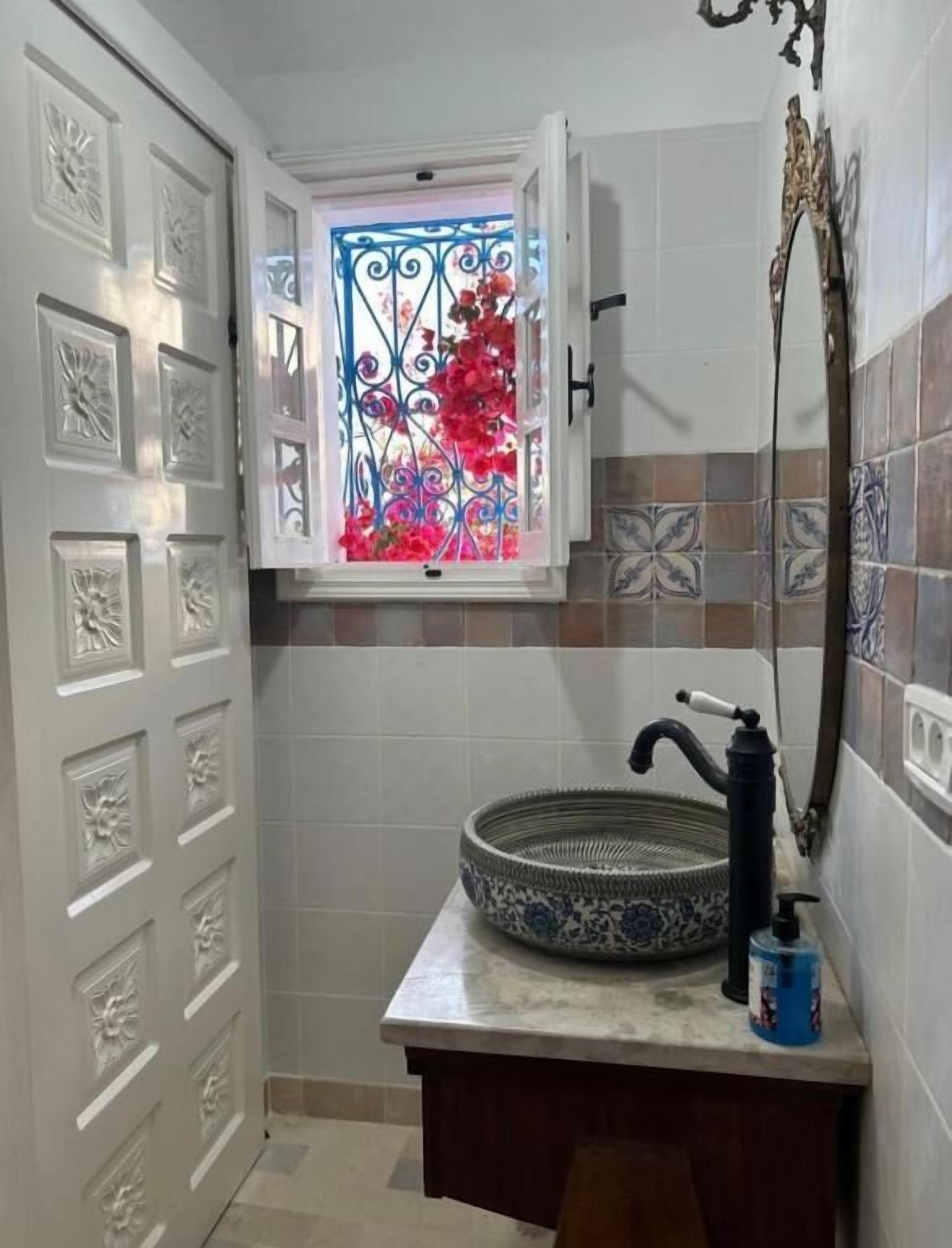 Un baño con un ventanal decorativo, un lavabo y un espejo.