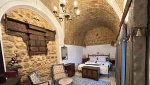 A room with stone walls, a bed with a headboard, a chandelier, and a patterned rug. - Guesthouse DarHamdoun (Hammam Al Agzaz)