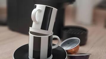 En kaffemaskine, en kop og en underkop på en træoverflade.