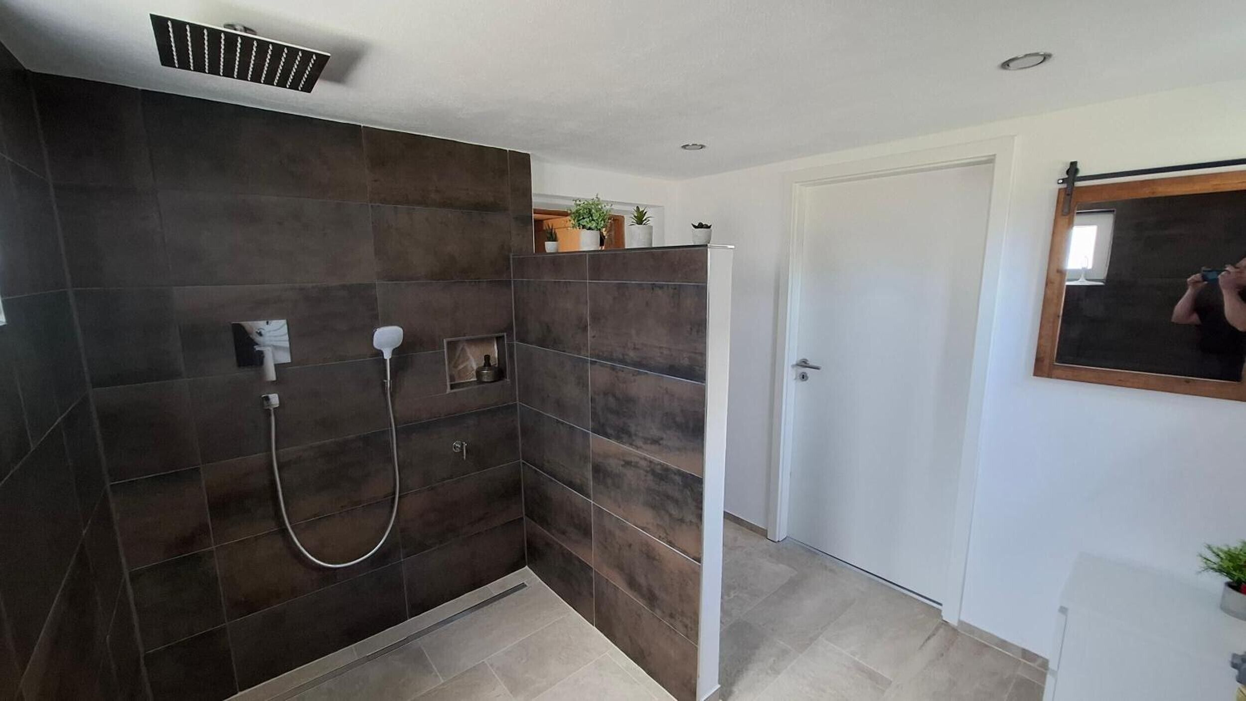 A modern bathroom with dark tiles, a shower, a toilet, and a mirror.