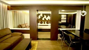 A modern living room with a sofa, a dining area with chairs, and a kitchen visible through an open doorway. - HOTEL RUBY PALACE (Tiruchirappalli)