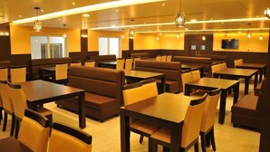 A restaurant with booths and tables, overhead lighting, and a television on the wall. - HOTEL RUBY PALACE (Tiruchirappalli)