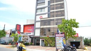A multi-story hotel with a modern facade, signage for a nearby restaurant, and a motorcycle parked in front. - HOTEL RUBY PALACE (Tiruchirappalli)