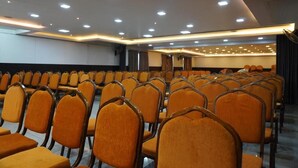 A conference room with rows of orange chairs, a stage, and a ceiling with recessed lighting. - HOTEL RUBY PALACE (Tiruchirappalli)