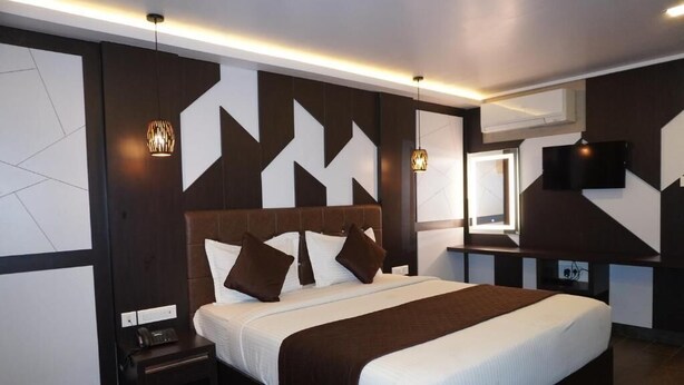 A modern hotel room with a large bed, a bedside table, a TV mounted on the wall, and a decorative wall panel. - HOTEL RUBY PALACE (Tiruchirappalli)