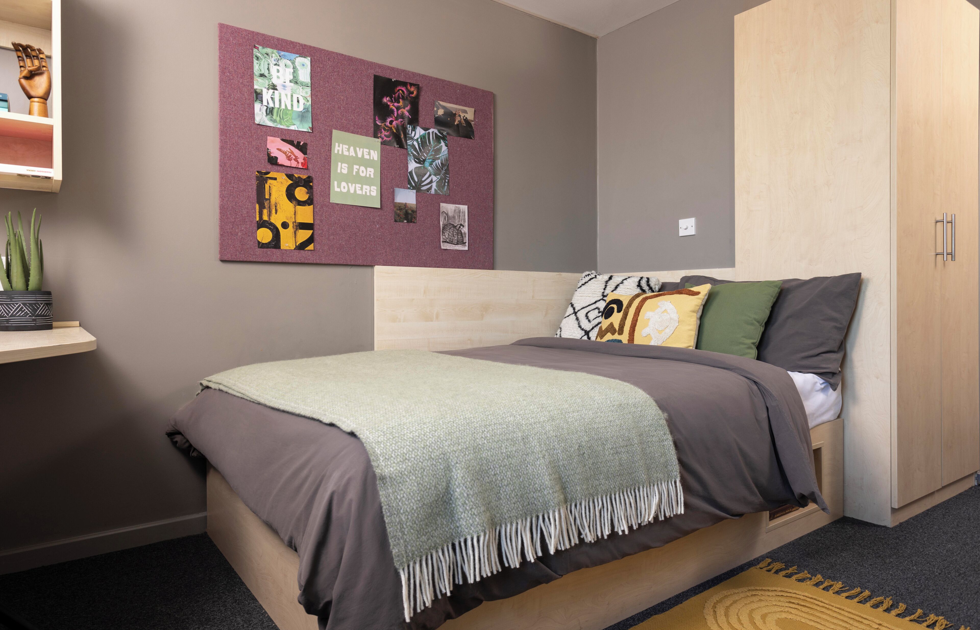 A bedroom with a bed, a bulletin board, a wardrobe, and a small shelf with plants.