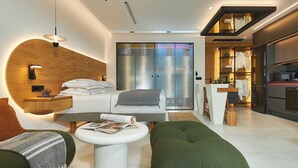 Ein modernes Hotelzimmer mit Bett, Nachttisch, Leseplatz, einer Küchenzeile und einer Glasschiebetür zum Balkon.