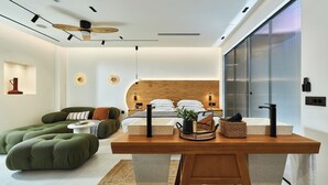 Ein modernes Schlafzimmer mit einem hölzernen Kopfende, einem Nachttisch, einem grünen Sofa und einem Essbereich mit einem Holztisch.