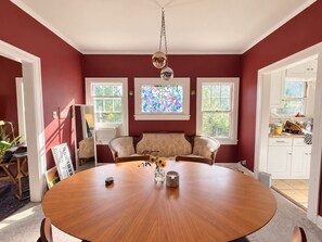 Ein Esszimmer mit einem runden Tisch, zwei Stühlen, einer Blumenvase und einer Kristallleuchter.