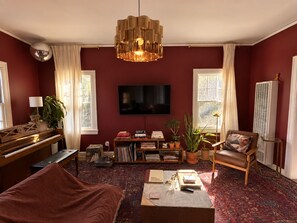 Ein Wohnzimmer mit einem Klavier, einem Fernseher, einem Sofa, einem Couchtisch und einem Kamin.