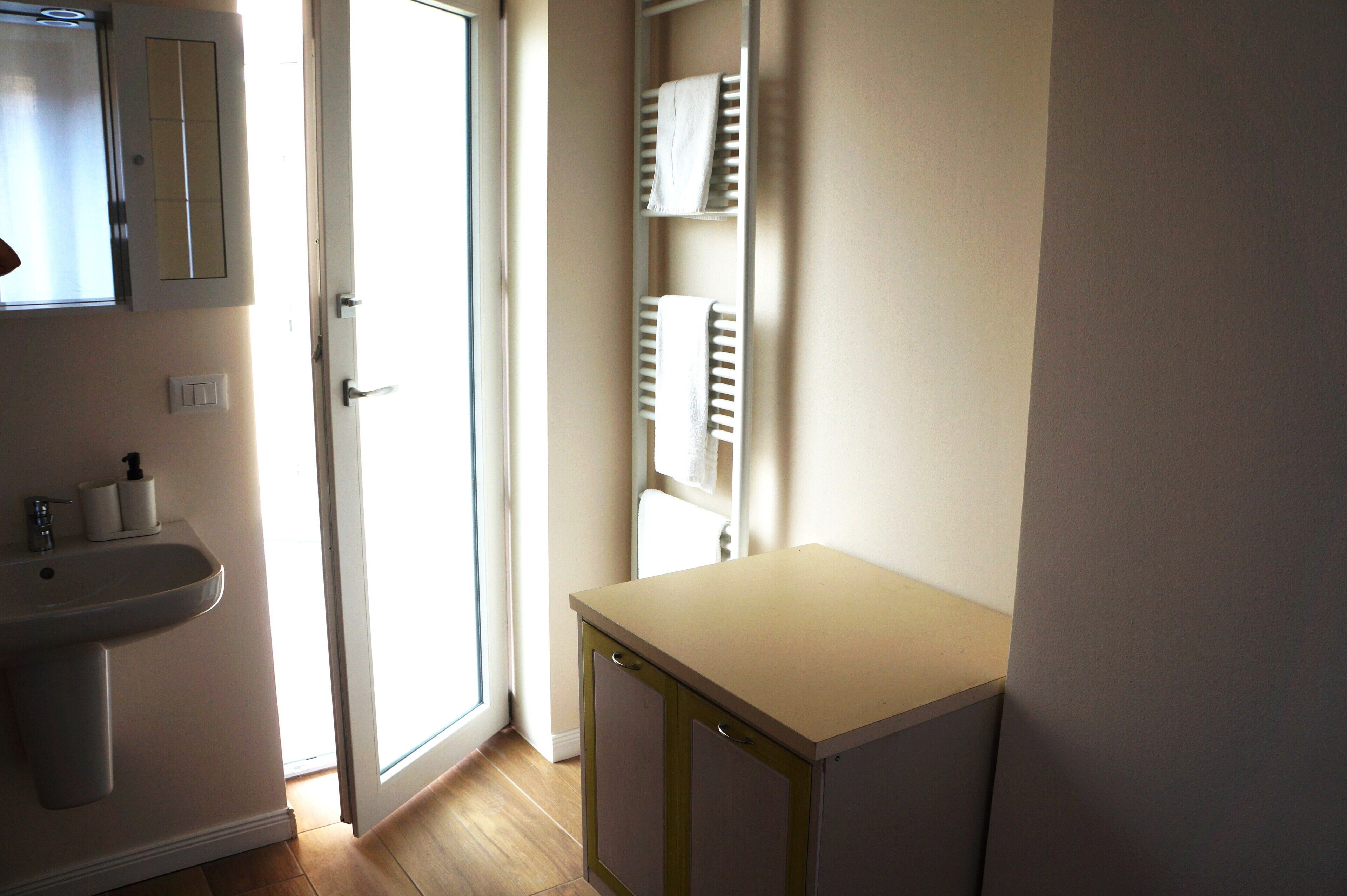 Een badkamer met een wastafel, een spiegel, een handdoekrek en een deur naar een andere kamer.