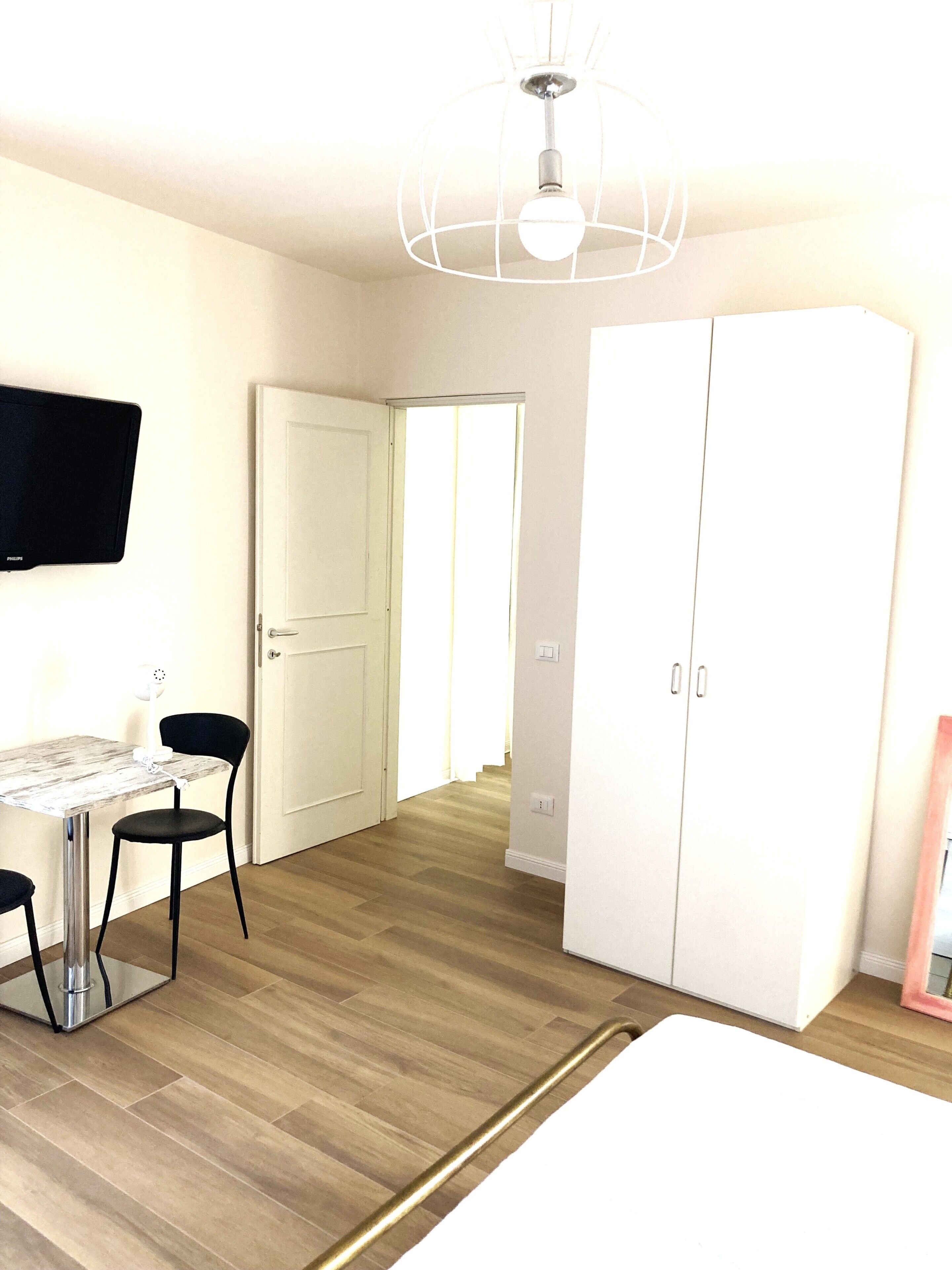 A bedroom with a bed, a desk with a chair, a wardrobe, and a television on the wall.