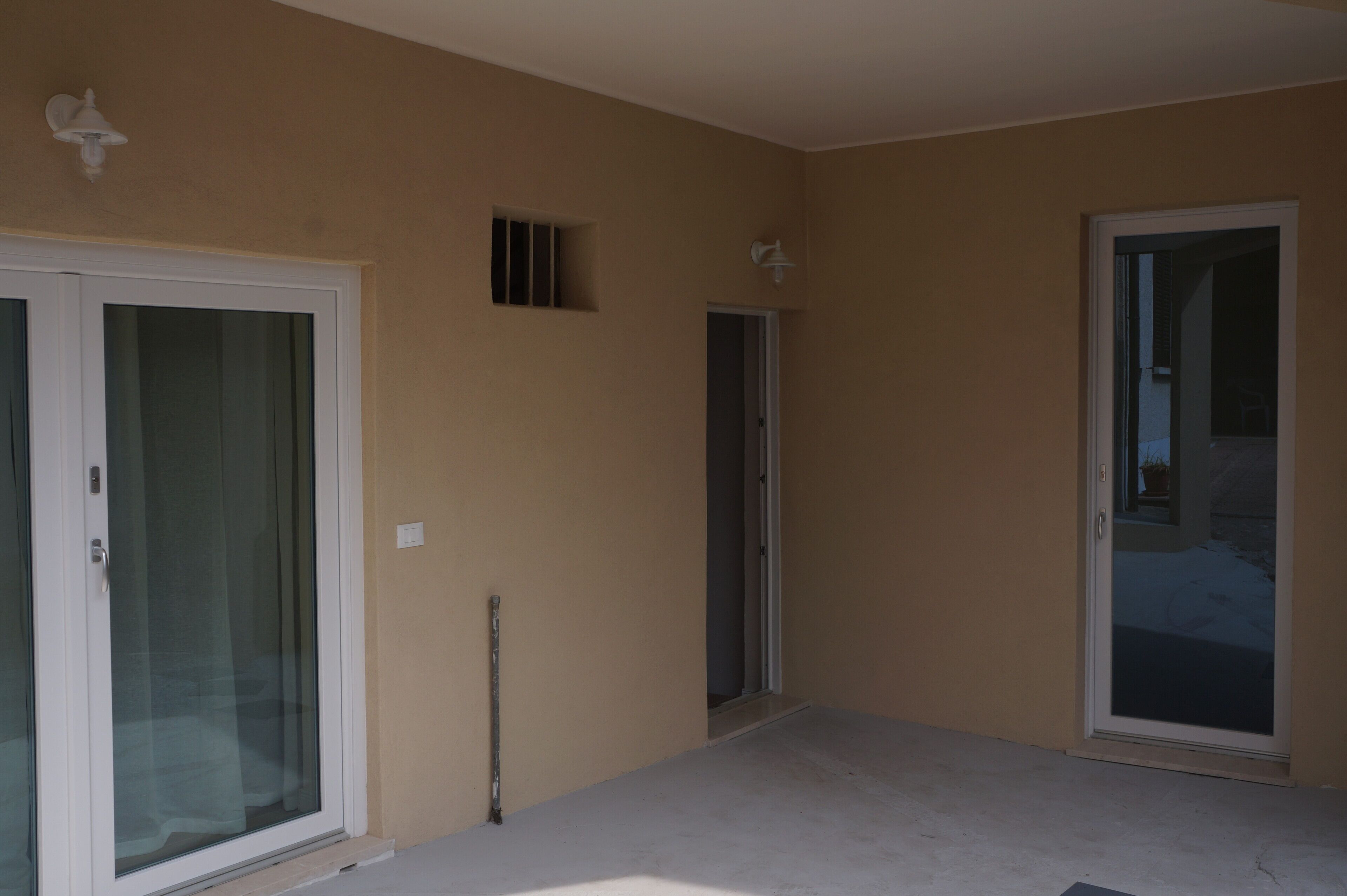 Ein Zimmer mit einer Schiebeglastür, einem kleinen Fenster und einer Tür zu einem anderen Raum.