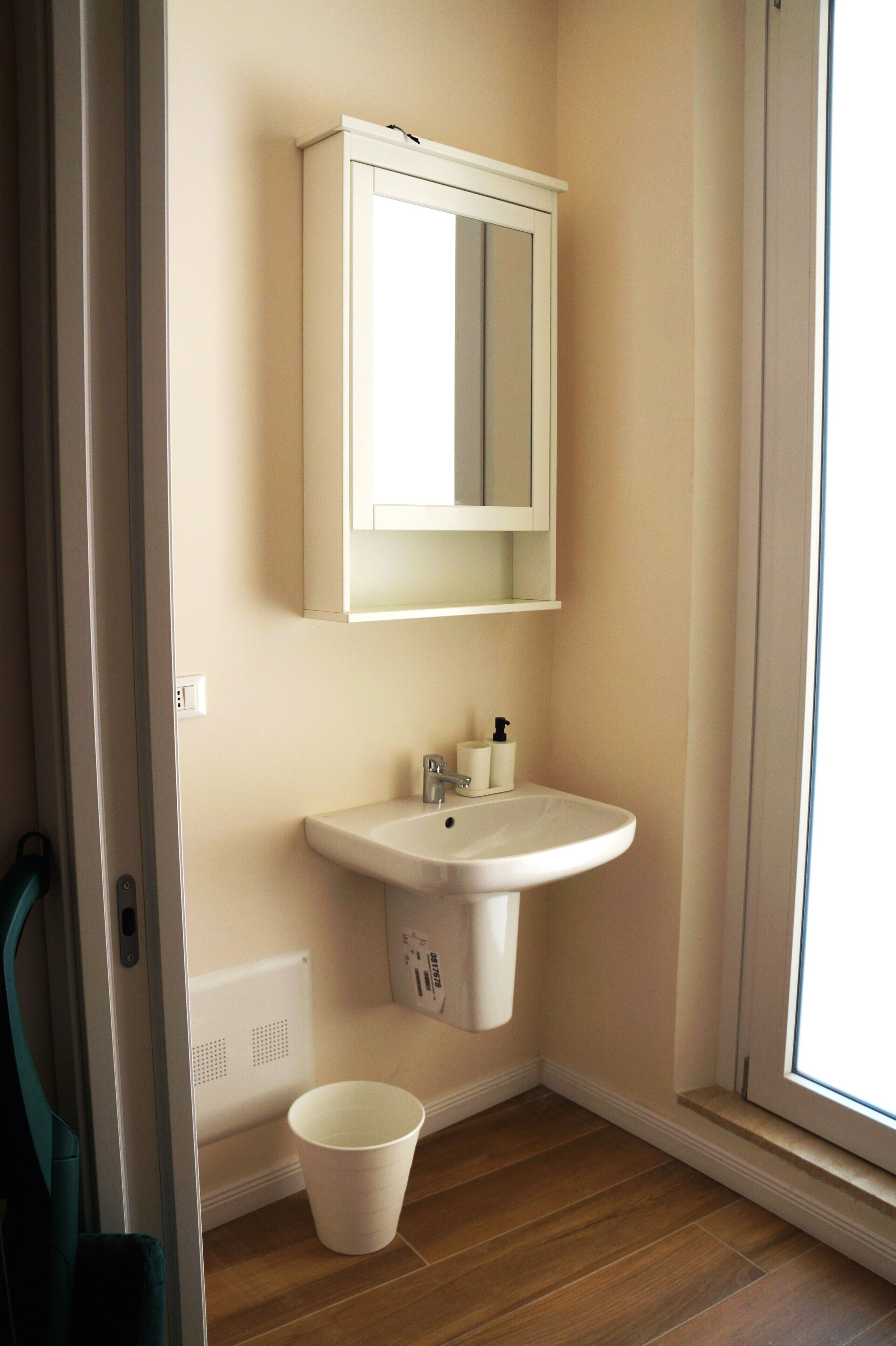 A bathroom with a white sink, mirror, and a white bucket on the floor.