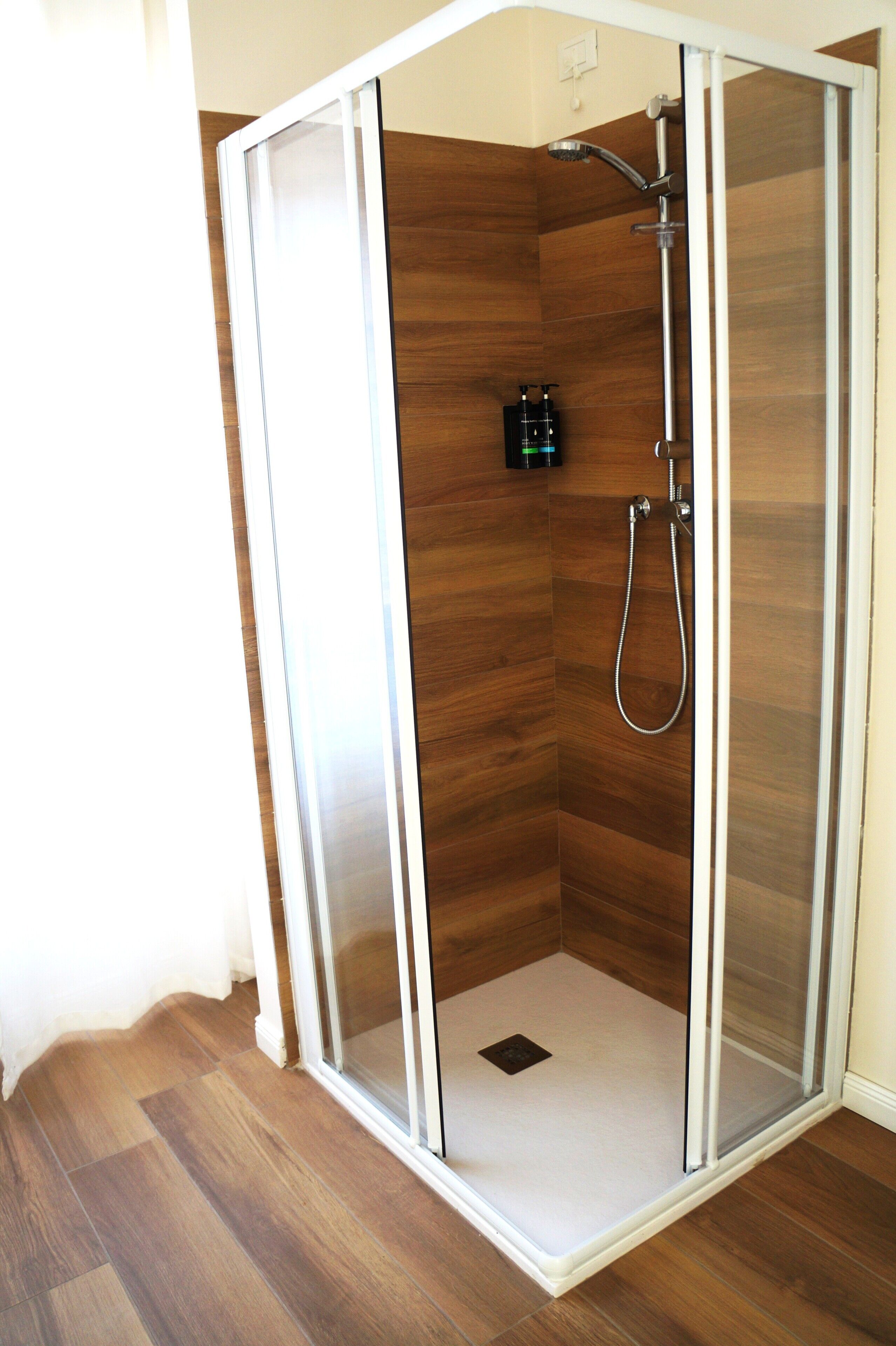 A glass-enclosed shower stall with a wooden floor and a showerhead.