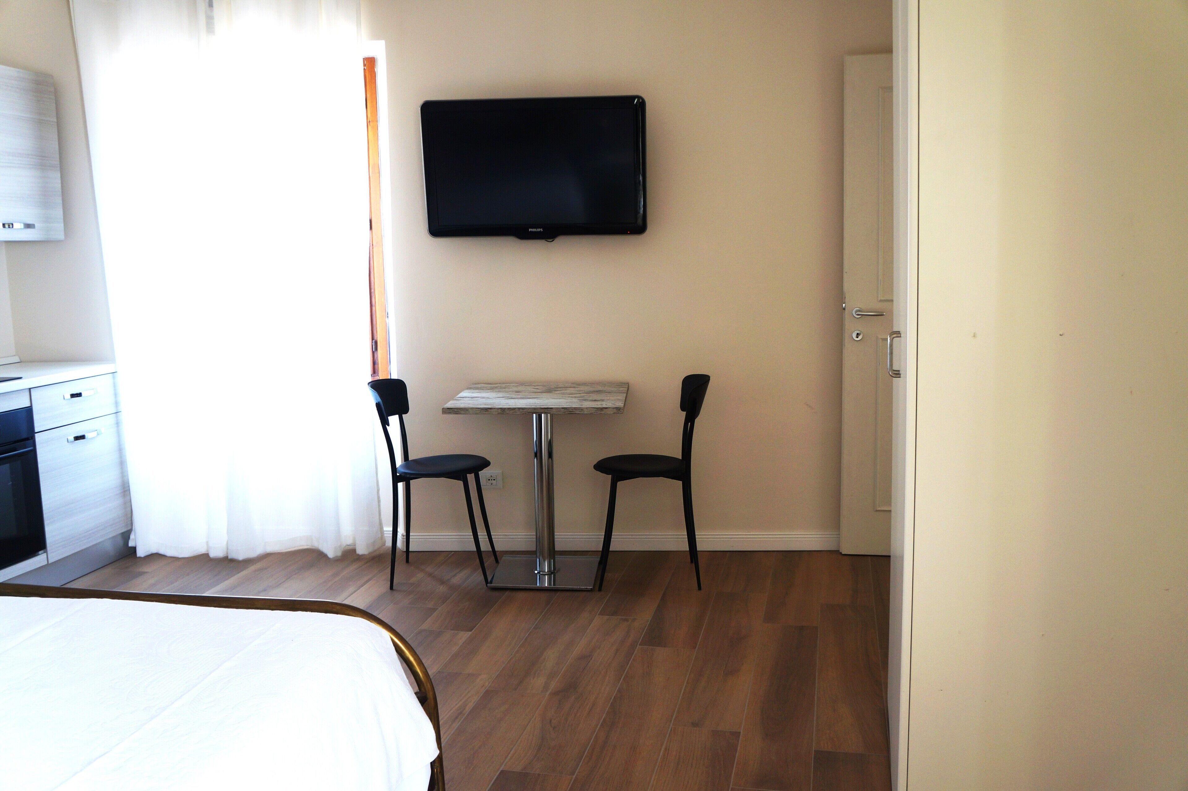 Une chambre d’hôtel avec un lit, une petite table, deux chaises, un téléviseur fixé au mur et une porte.