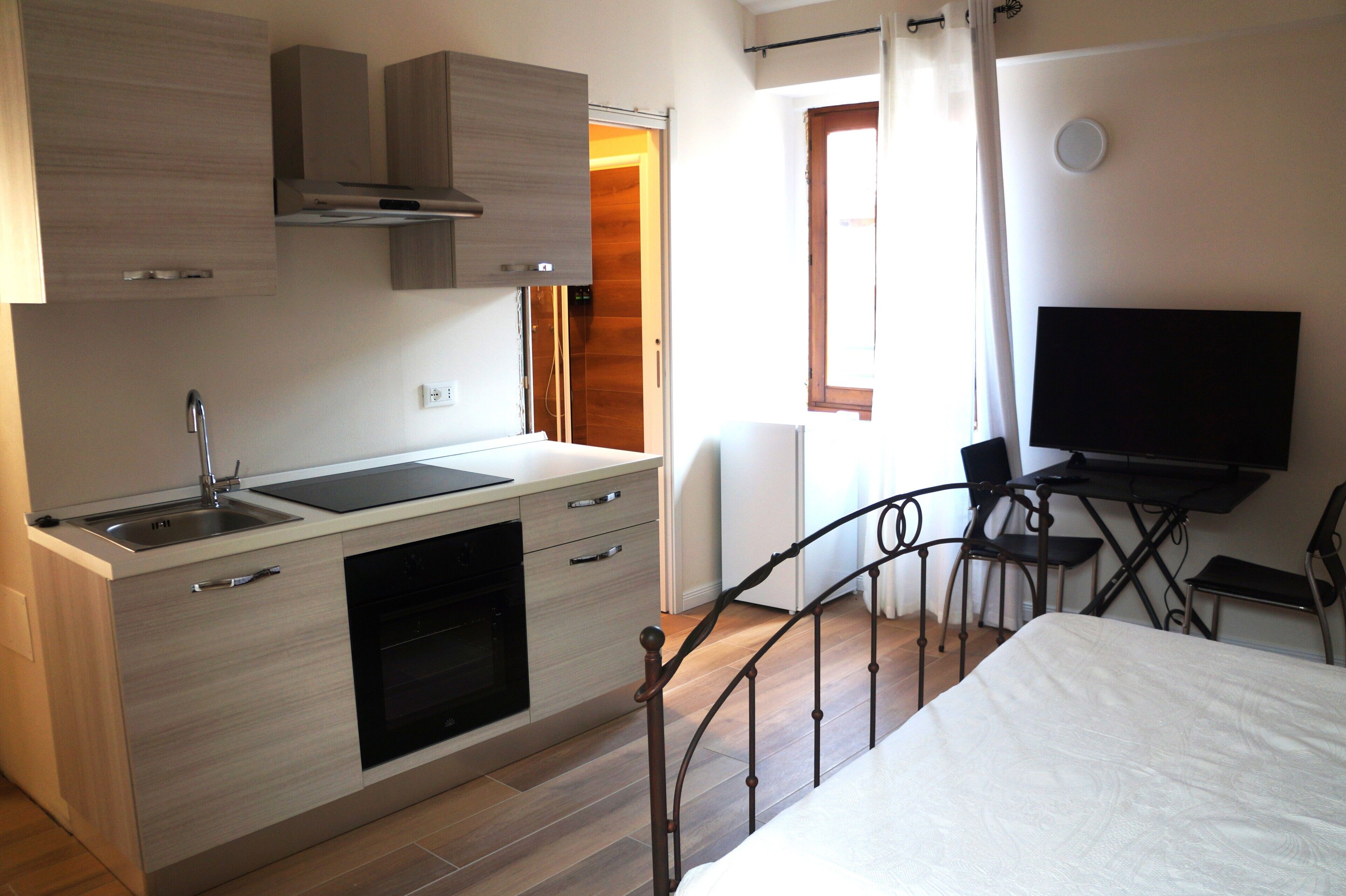 A compact kitchenette with a sink, stove, and cabinets, a small dining area with a table and chairs, and a bed with a white comforter.