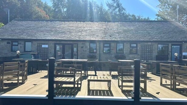 Un edificio con fachada de piedra, varias ventanas y una terraza de madera con bancos.