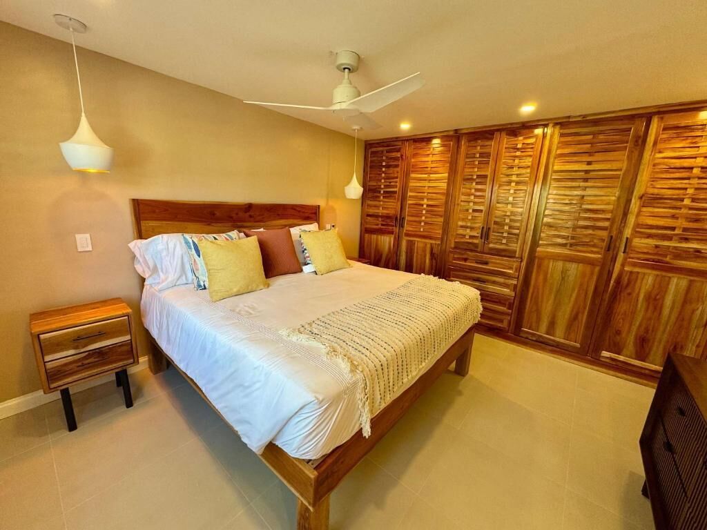 A bedroom with a bed, wooden wardrobe, nightstand, and ceiling fan.