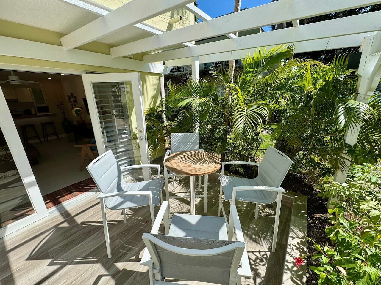 Um pátio externo com pérgola branca, uma mesa redonda e quatro cadeiras brancas.