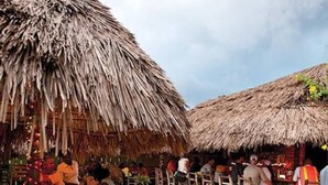 Un área de comedor al aire libre con sombrillas de paja y taburetes de madera.