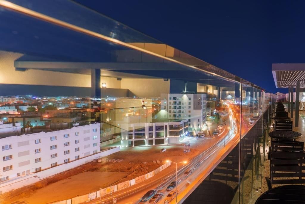 A modern building with a glass facade, a covered outdoor area, and a busy street below.