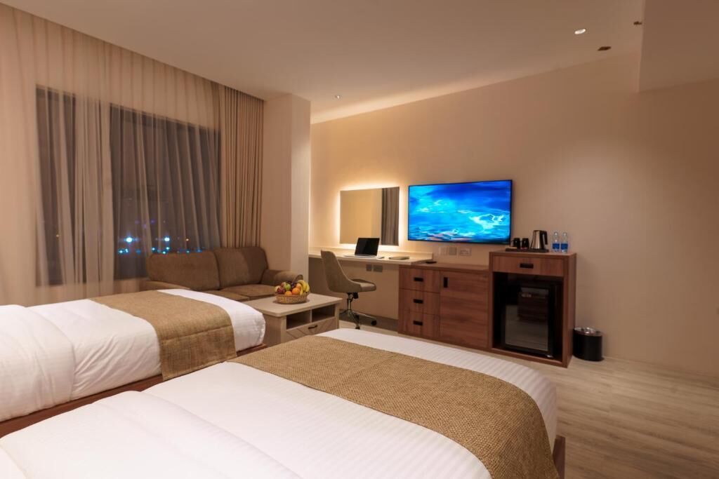 Une chambre d’hôtel avec deux lits, un bureau, une télévision et une vue sur la ville la nuit.