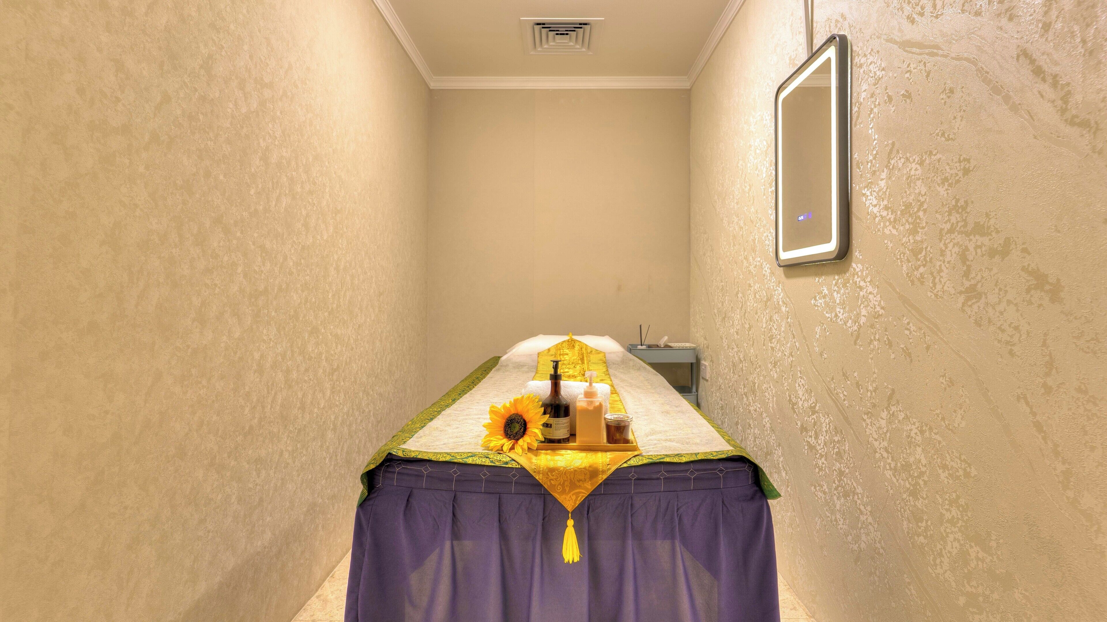 A narrow room with a bed, a mirror, and a small table with toiletries.