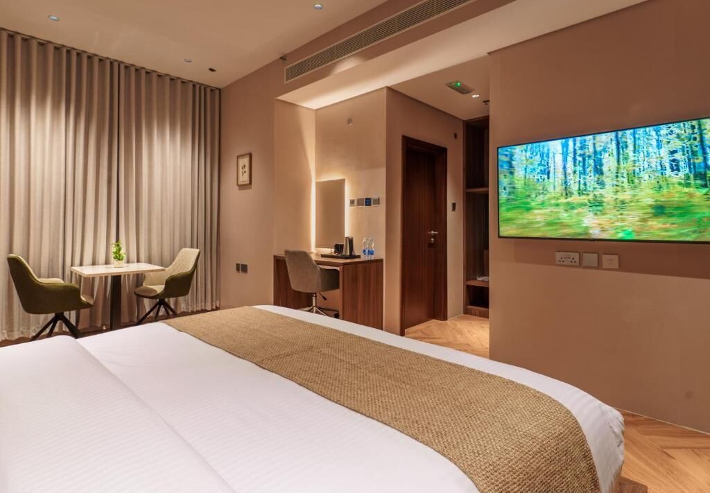 Een hotelkamer met een groot bed, een bureau, een stoel, een televisie en uitzicht op een bos.