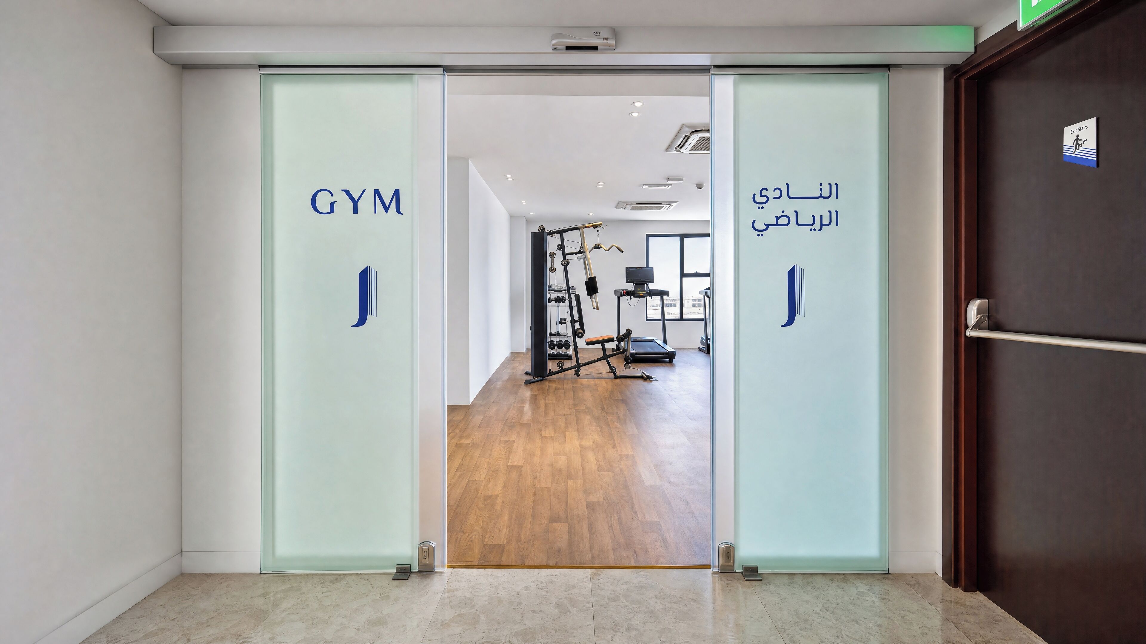 Ein Fitnessstudioeingang mit Glastüren, Laufbändern und Kraftgeräten.