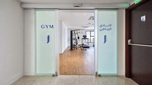 A gym entrance with glass doors, a treadmill, and weight machines.
