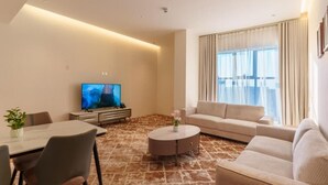 A modern living room with a flat-screen TV, a sofa, a dining table with chairs, and a coffee table.