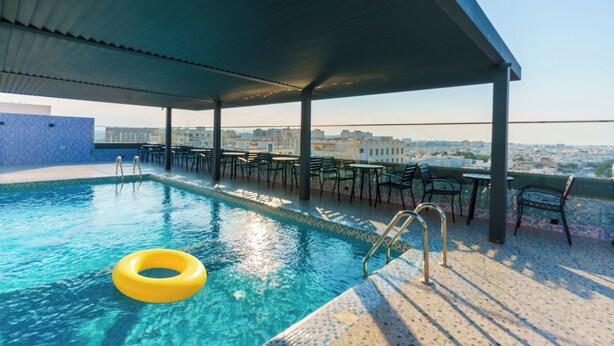A rooftop pool with clear blue water, a yellow float ring, and outdoor seating under a covered area.