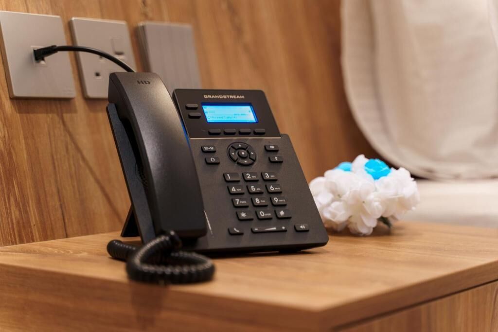A Grandstream phone on a wooden table with a flower arrangement beside it.