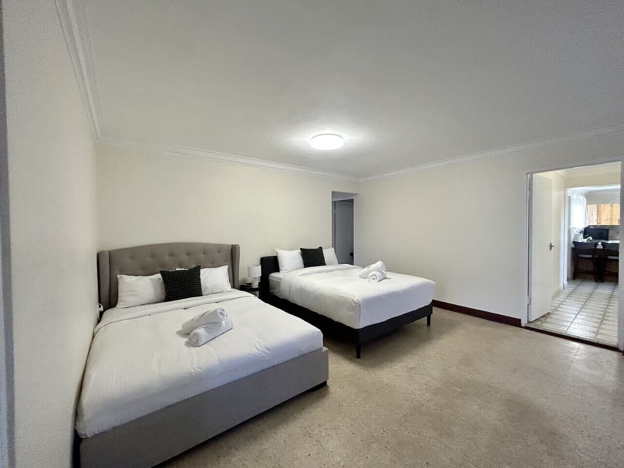 A hotel room with two beds, a ceiling light, and a door leading to a bathroom.