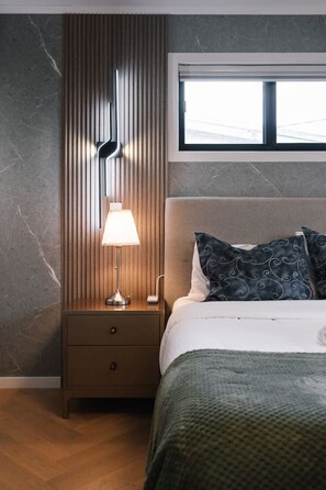 A modern bedroom with a bed, a nightstand with a lamp, and a window. - Affordable Family Retreat | Pool & Prime Location (MacGregor)