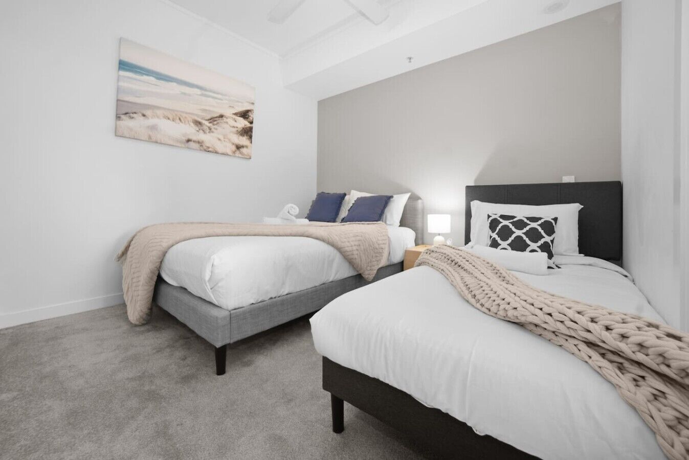 A bedroom with two beds, a nightstand, a lamp, and a painting on the wall.