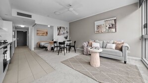 Ein modernes Wohnzimmer mit grauem Sofa, einem Esstisch mit Stühlen, einer Küchenzeile mit Schränken und einem Deckenventilator.