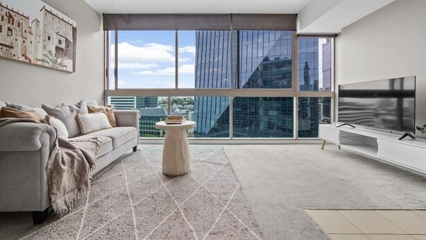 Ein modernes Wohnzimmer mit einer Couch, einem Couchtisch, einem Fernseher und großen Fenstern mit Blick auf die Stadt.
