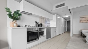 Eine moderne Küche mit weißen Schränken, einem eingebauten Backofen, einer Mikrowelle und einem Geschirrspüler. Auf der Arbeitsplatte steht ein Blumentopf und an der Wand hängt ein Bild.