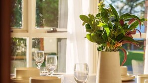 Een eettafel gedekt met borden, kommen en wijnglazen, met een potplant in het midden.