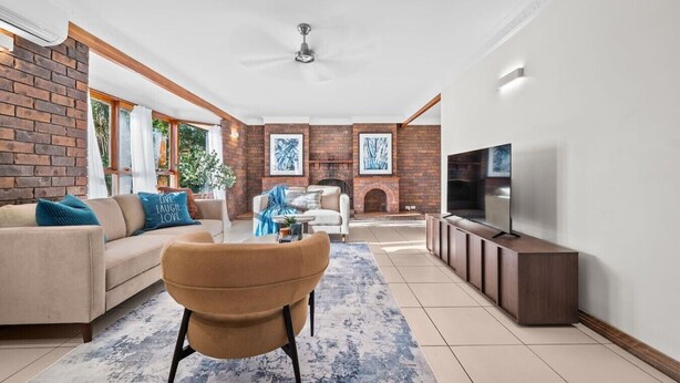 Een woonkamer met een bank, fauteuil, open haard, televisie en een bakstenen muur.