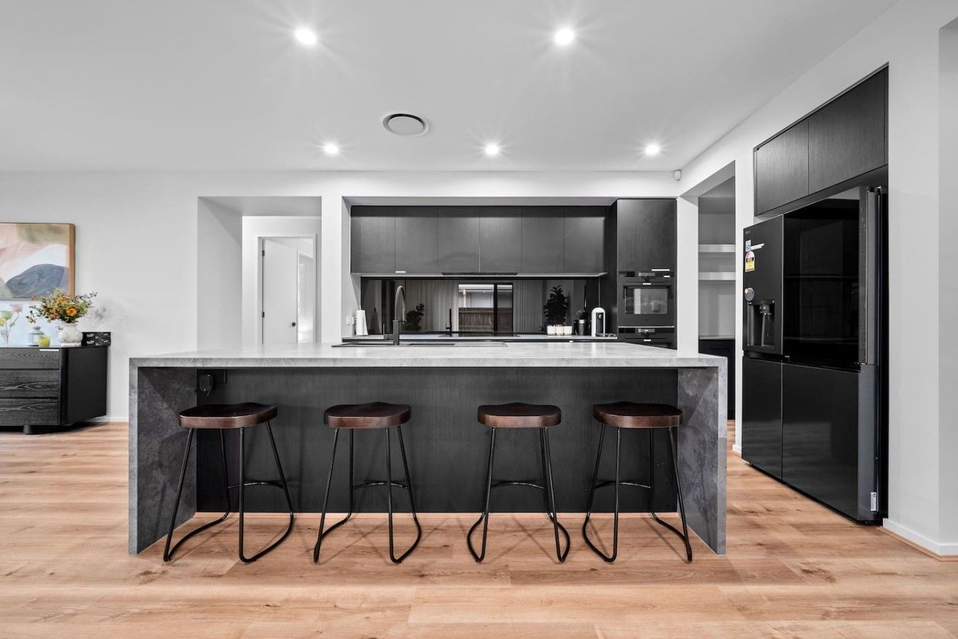 A modern kitchen with a central island, bar stools, and a black refrigerator.