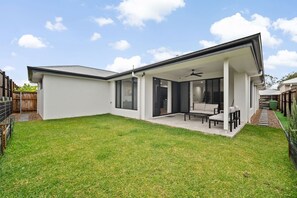 Una casa moderna con un patio cubierto, césped y un patio trasero cercado.