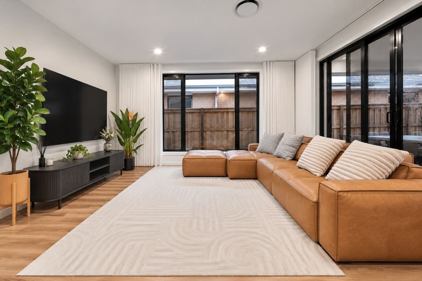 Una sala de estar moderna con un sofá modular, un televisor de pantalla plana y ventanas amplias.